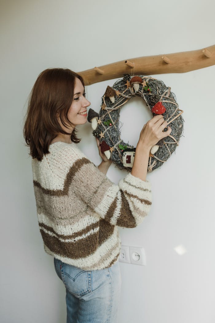 Smiling woman hanging a decorated wreath indoors, creating a festive atmosphere.