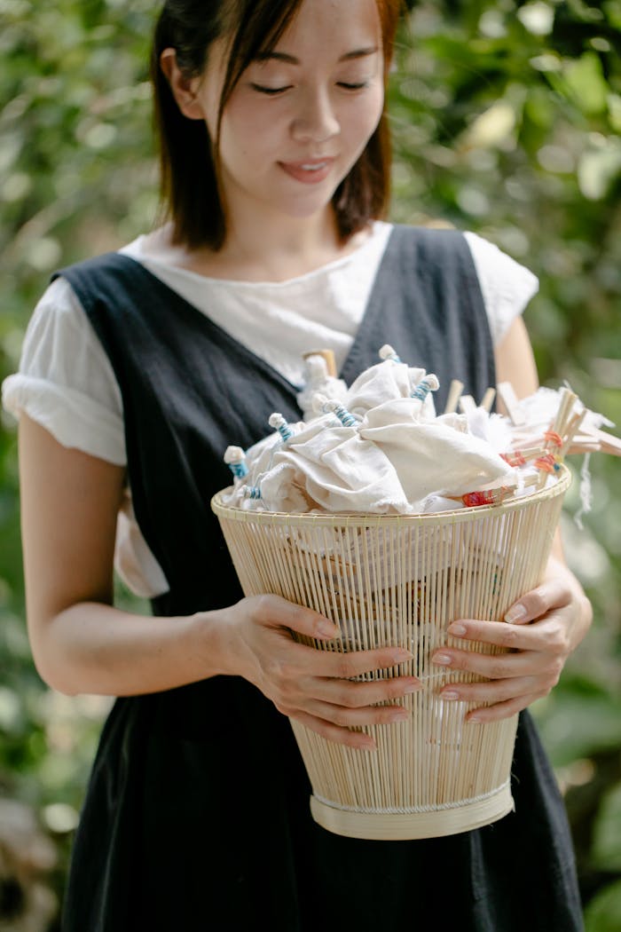 Asian woman outdoors holding a basket of tie-dye cloths, smiling and cheerful.